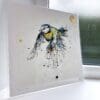 A print of Coat of Colour by Kathryn Callaghan, which features a blue tit in flight. The 30cm print is presented flat in a clear cello bag with a golden KC sticker in the top right.