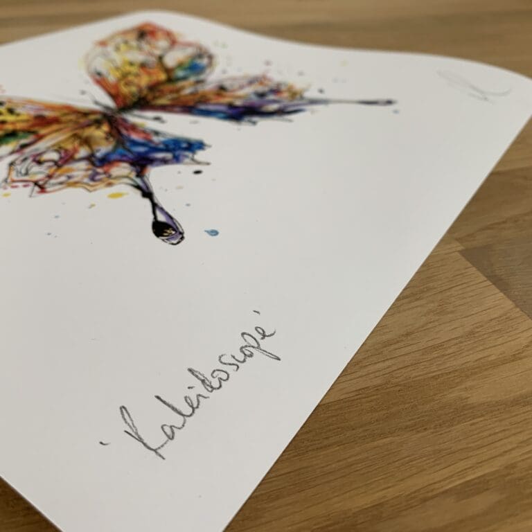 Photograph of Kaleidoscope by Kathryn Callaghan, a print of a magnificent butterfly with wings of orange, green, blue, and purple, which shows the print's title handwritten in the bottom left corner and the artist's signature in the bottom right, with space between to add a custom personalisation.