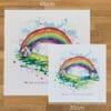 Two prints of Under the Same Rainbow by Kathryn Callaghan, a print of an arched rainbow curving between two houses, to show the size difference between the 45cm print and the 30cm print.