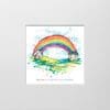 A digital mockup showing how a miniature print of Under the Same Rainbow by Kathryn Callaghan will look presented in a 23cm mount. Under the Same Rainbow features a rainbow arching between two houses with digitally added text below reading "We are all under the same rainbow".