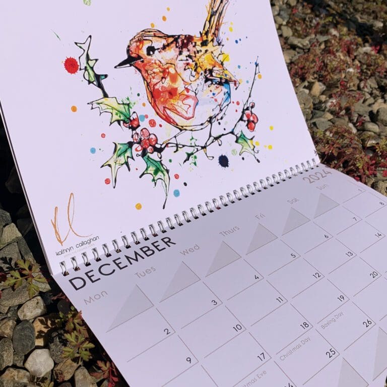 The 2024 Kathryn Callaghan Fine Art Calendar, open to show December's month art of a robin on a holly branch.