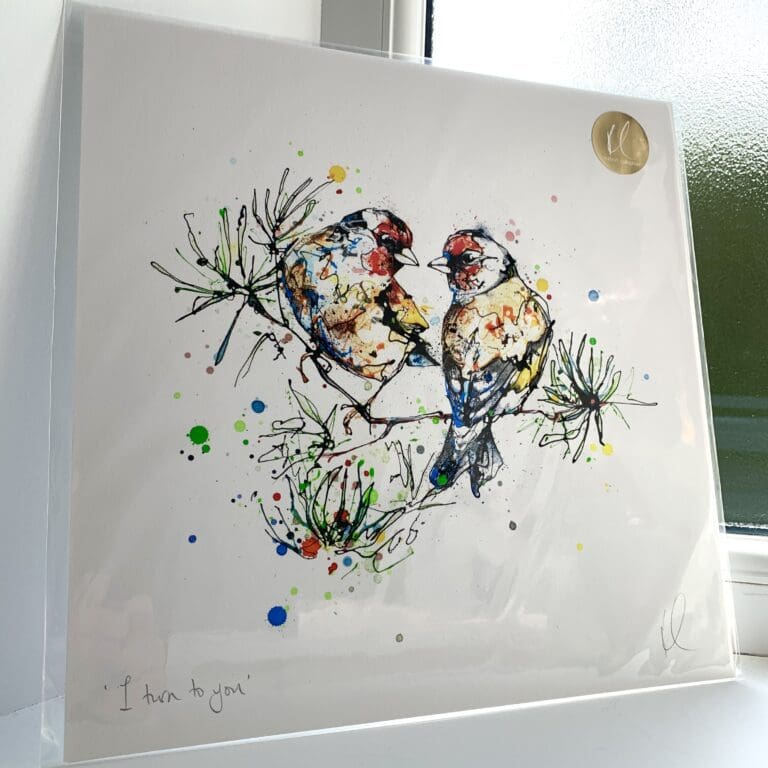 A print of I Turn To You by Kathryn Callaghan, which features a pair of goldfinches sitting together on a fir branch. The 30cm print is presented flat in a clear cello bag with a golden KC sticker in the top right.