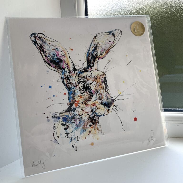 A print of Hartley by Kathryn Callaghan, which features a cheerful hare's face. The 30cm print is presented flat in a clear cello bag with a golden KC sticker in the top right.