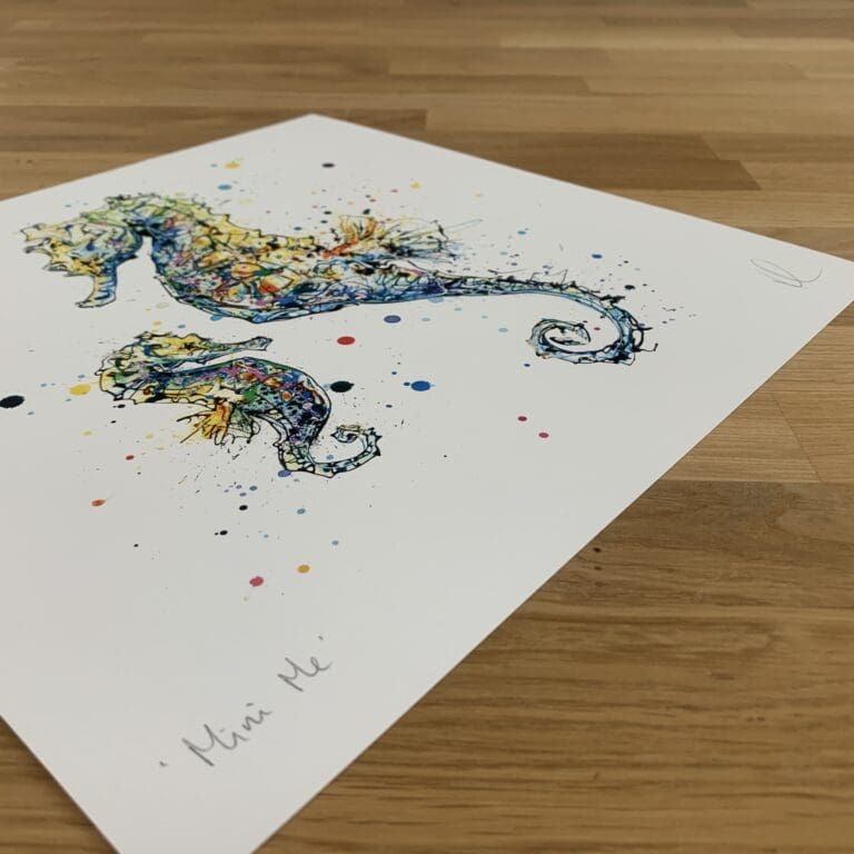 Photograph of Mini Me, a print of an adult and baby seahorse in tones of green, blue and yellow by Kathryn Callaghan, which shows the print's title handwritten in the bottom left corner and the artist's signature in the bottom right, with space between to add a custom personalisation.