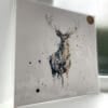 A print of Nightfall by Kathryn Callaghan, which features a stag standing gazing at the viewer, lit in tones of dark blue and gold. The 30cm print is presented flat in a clear cello bag with a golden KC sticker in the top right.