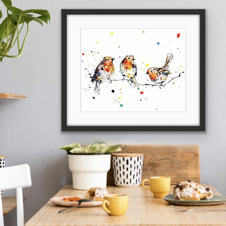 Close To You Limited Edition print of three robins on a branch displayed in a black frame above a kitchen table