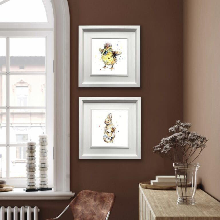 Two prints are hung vertically in Deluxe White Frames in a warm brown room beside a window and flowers. The prints are of a duckling named Sherbet and a baby rabbit named Pumpkin.