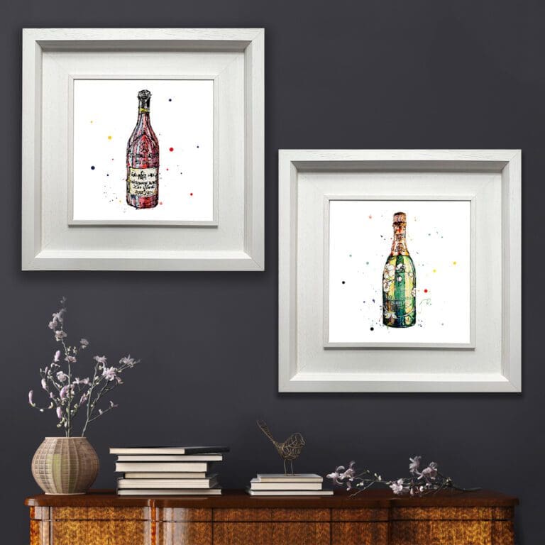 Two Prints shown in Situ on a dark blue wall above a wooden sideboard with books and lavender. The prints are of a bottle of red Chateauneuf du Pape wine and Belle Eopque champagne. They are both in Deluxe White Frames.