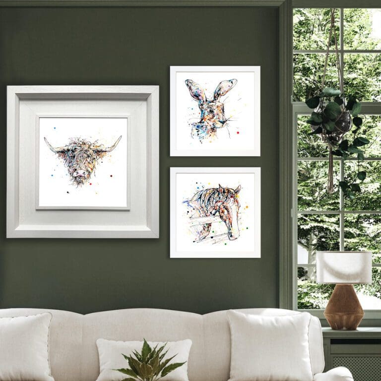 Three prints shown in white frames in situ on a dark green wall above a white sofa. The prints are Harris, which portrays the face of a highland cow in a deluxe white frame, Hartley, which shows the face of a hare in a standard white frame, and Hudson, which depicts the face of a horse in a standard white frame.