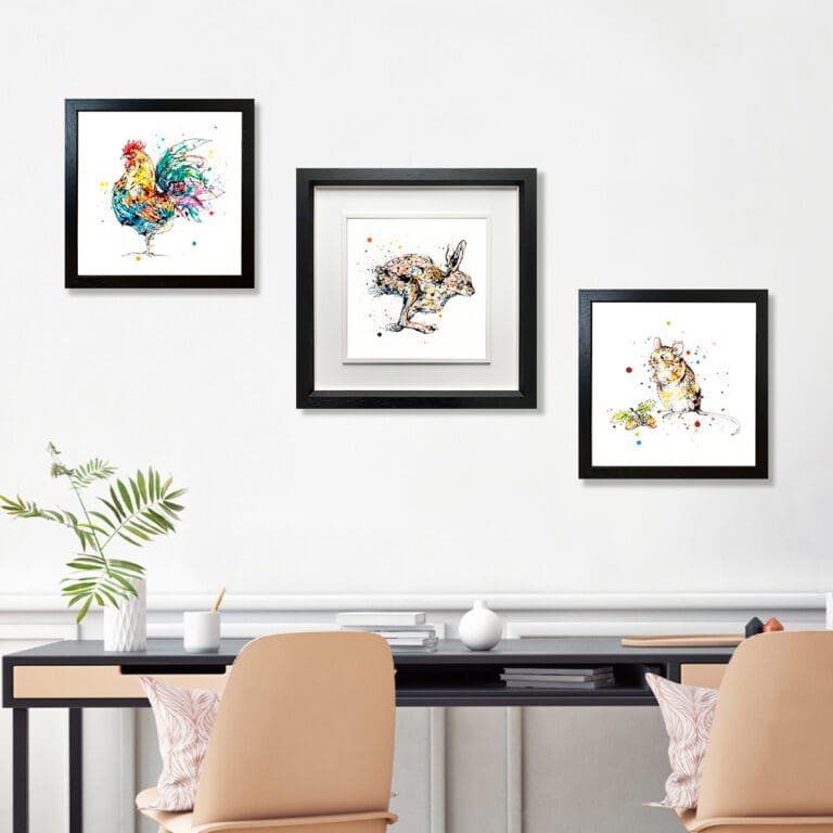 Three prints shown in black frames in situ on white wall above a desk. The prints are Clarence which depicts a cockerel in a standard black frame, Like The Wind which features a running hare in a deluxe black frame, and Little Guy, which depicts a mouse in a standard black frame.