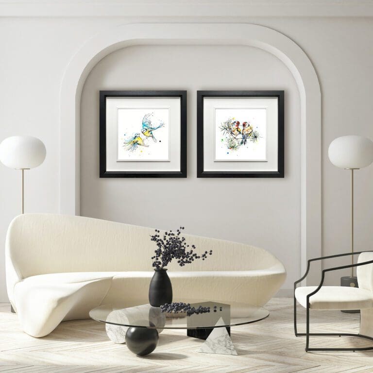 Two prints shown in Deluxe Black Frames in a recessed wall space in a white room with cream sofa and houseplant. The prints are United, which depicts two blue tits in flight, and I Turn To You, which depicts two goldfinches looking at one another.