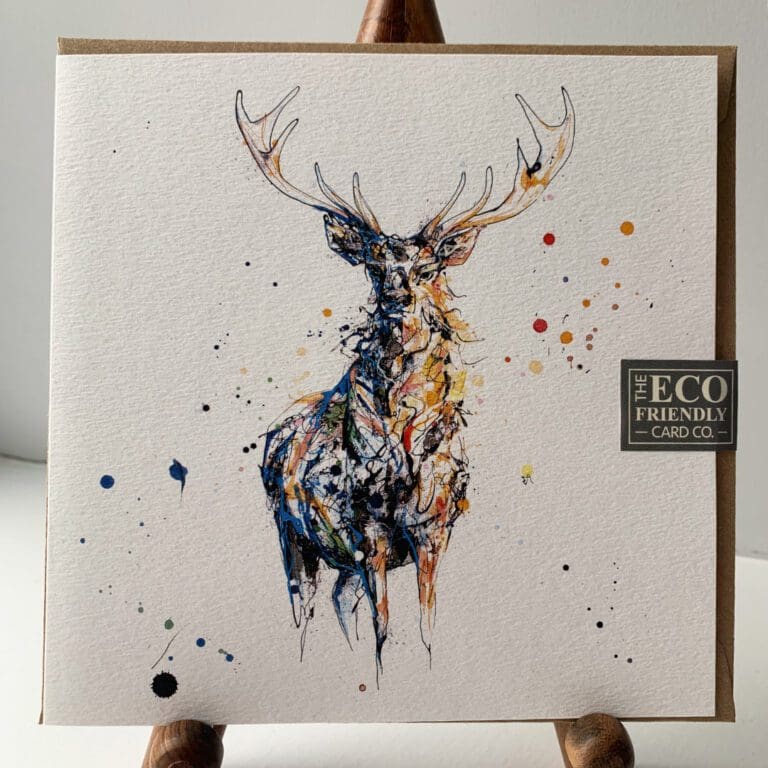 Greetings card featuring a poured painting of a stag by Kathryn Callaghan. The stag is gold and amber shadowed in black and dark blue. It is surrounded by splashes of dark blue and orange, and comes with a brown recycled envelope. A sticker on the card reads "The Eco Friendly Card Company".