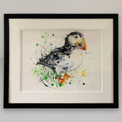 Bashful Original Puffin Painting by Kathryn Callaghan shown in a traditional black frame with double mount on a white wall