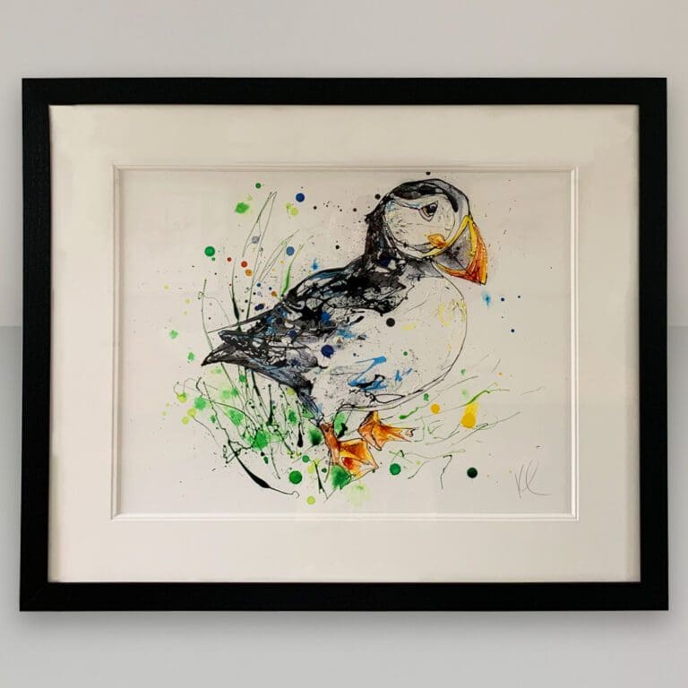 Bashful Original Puffin Painting by Kathryn Callaghan shown in a traditional black frame with double mount on a white wall