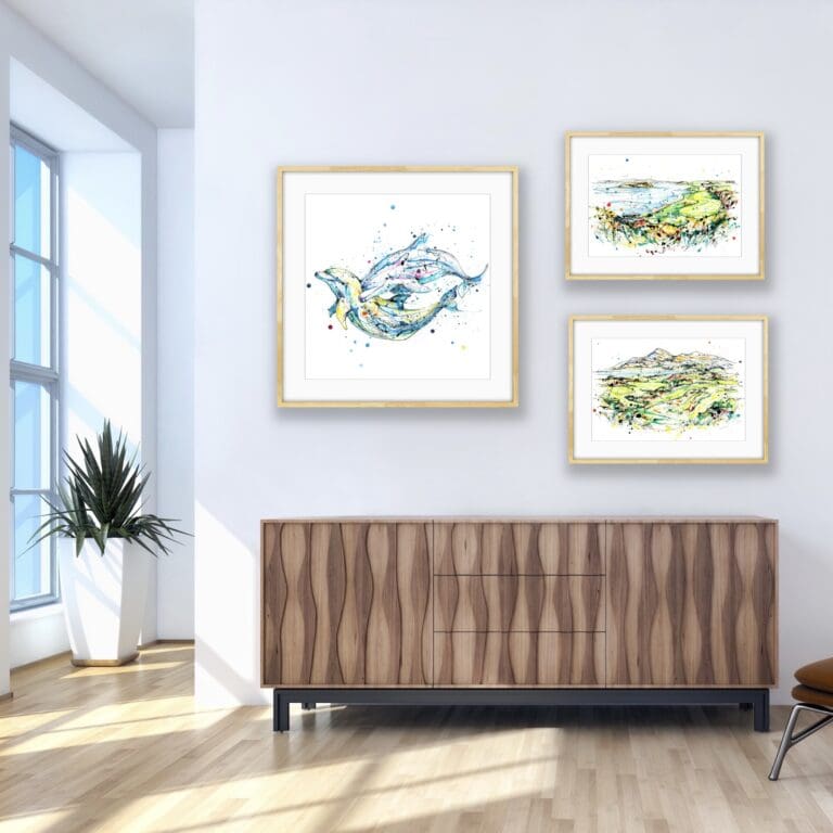 A framed print of Splash which features two swimming dolphins, and two framed prints of golf courses called 4th Royal County Down and Coney Island are all shown in situ above a wooden sideboard with a window to the left.