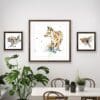 Treasure Hunt, a fox print, is flanked by Like the Wind, a print of a running hare, and Airborne, a print of a robin in flight, above a dining table surrounded by plants.