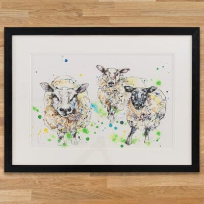 All Ears Original Sheep Painting by Kathryn Callaghan, framed in a classic black frame with double white mount set on a wooden worktop.