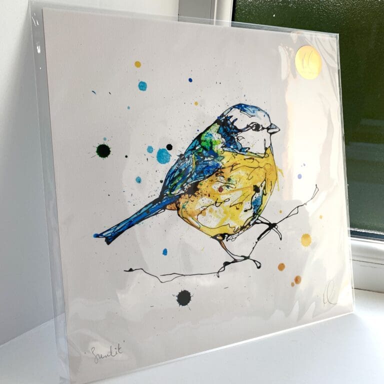 A print of Sunlit by Kathryn Callaghan, which features a bright blue tit posed on a thin branch. The 30cm print is presented flat in a clear cello bag with a golden KC sticker in the top right.