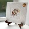A miniature print of Get Set, Go! by Kathryn Callaghan, which features a red squirrel poised to run. The print is presented mounted at 23cm, in a clear cello bag with a gold KC sticker in the top right corner, and is displayed here on a small wooden easel in a windowsill.