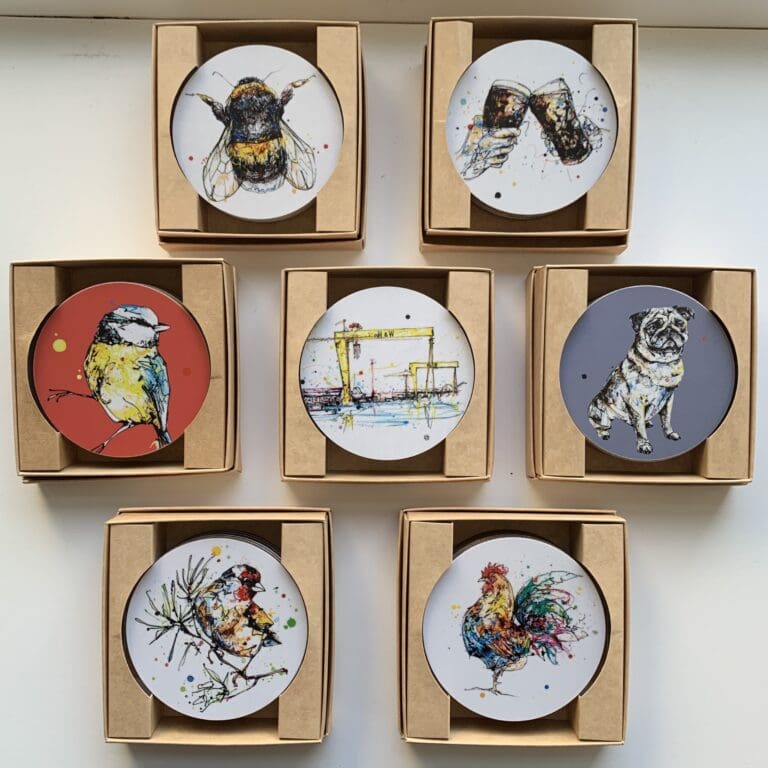 Seven sets of coasters in display boxes, featuring artwork by Kathryn Callaghan. The seven sets feature designs of bees, Irish drinks, garden birds on colourful backgrounds, Northern Irish landmarks, dogs on purple backgrounds, garden birds on white backgrounds, and farmyard animals.