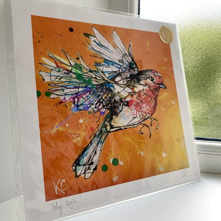 A print of Fly High by Kathryn Callaghan, which features a robin in flight against a bright orange and yellow background. The 30cm print is presented flat in a clear cello bag with a golden KC sticker in the top right.