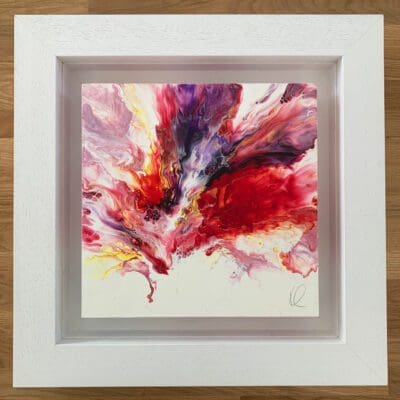 An original abstract painting by Kathryn Callaghan, named Passion. The painting features a swell of red, purple, yellow, and pink paint blown from the lower third of the surface board, and is framed in a deep floating white wood frame.