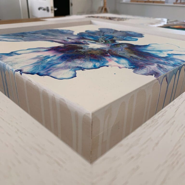 A close up photograph showing the deep floating tray frame surrounding Revival, an original abstract painting by Kathryn Callaghan. The depth of the frame allows the edges of the wooden surface to be visible, where some of the blue and white paint has spilled over the sides.