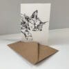 A notecard featuring a print of a sleeping cat named Dreamer by Kathryn Callaghan, accompanied by its recycled paper envelope.