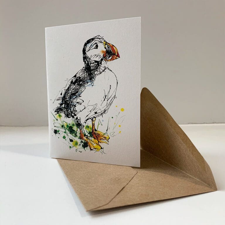 A miniature notecard featuring a print of a puffin by Kathryn Callaghan, entitled Atlantic Puffin. The card sits open on a brown envelope.