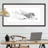 The Púca, a print of a mischievous creature from Irish folklore by Kathryn Callaghan, shown framed in situ in a neat office behind a desk with a MacBook, wooden chair, and gold floor lamp.