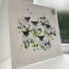 A print of Baa by Kathryn Callaghan, which features a flock of Scottish Blackface sheep looking curiously at the viewer. The 30cm print is presented flat in a clear cello bag with a golden KC sticker in the top right.