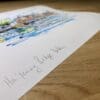 Photograph of Ha'penny Bridge Dublin, a print of a flock of sheep by Kathryn Callaghan, which shows the print's title handwritten in the bottom left corner and the artist's signature in the bottom right, with space between to add a custom personalisation.