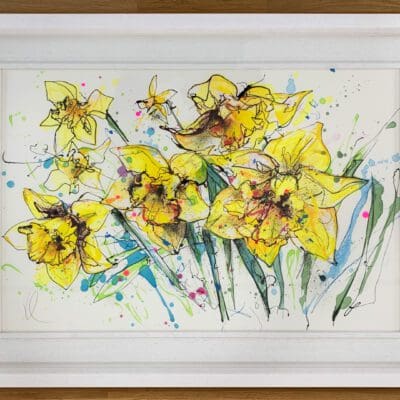 An original painting of a spray of daffodil flowers by Kathryn Callaghan. The painting is framed in a white wooden box frame and lays flat on a wooden tabletop.