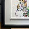 The bottom left corner of Just Hanging Around, an original painting by Kathryn Callaghan, which shows the two part white and black wooden frame and the artist's signature on the painting.