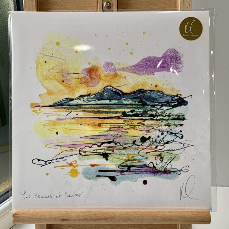 A print of The Mournes at Sunset by Kathryn Callaghan, which features a view of the Mourne Mountains with a purple and golden sunset in the background. The 30cm print is presented flat in a clear cello bag with a golden KC sticker in the top right.