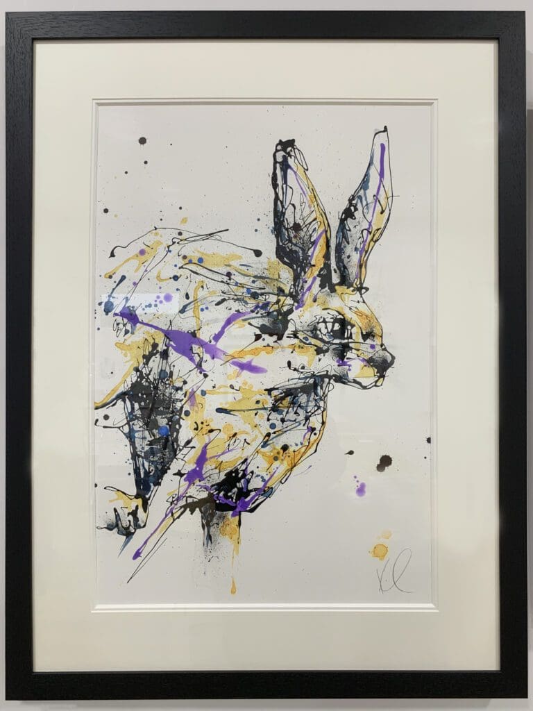 An original painting of a running hare by Kathryn Callaghan, with an off white mount and a black frame.