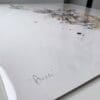 An angled close up photograph of the hand-written title present on Aura, a stag print by Kathryn Callaghan.