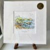 A miniature print of Causeway Rocks by Kathryn Callaghan, which features the Giants Causeway. The print is presented mounted at 23cm, in a clear cello bag with a gold KC sticker in the top right corner, and is displayed here on a small wooden easel in a windowsill.